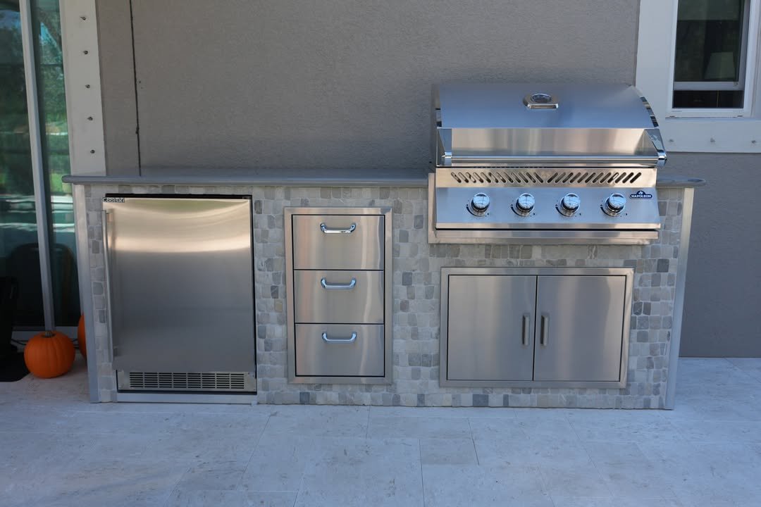 Finished outdoor kitchen with built-in grill, stainless storage, refrigerator, stonework, and counter space